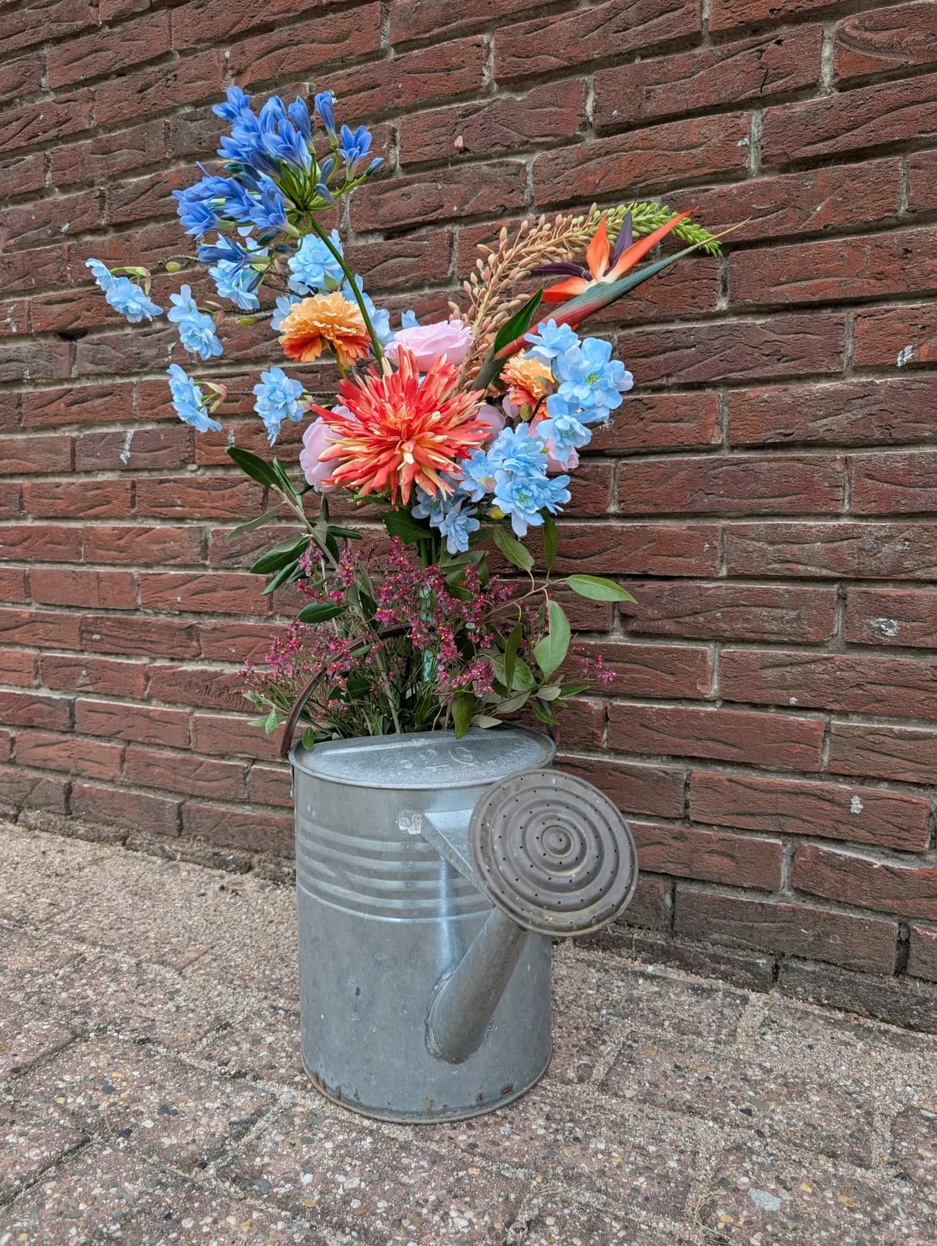 Bloemstuk in een metalen gieter met een combinatie van zijden en echte bloemen